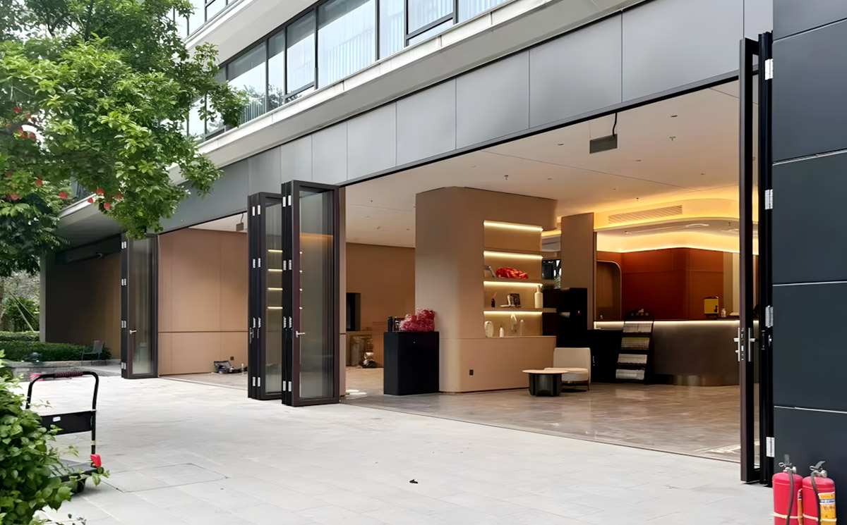 Heavy-duty, multi-panel aluminum folding glass doors creating a massive open entrance for a commercial luxury space Heavy-duty, multi-panel aluminum folding glass doors creating a massive open entrance for a commercial luxury space