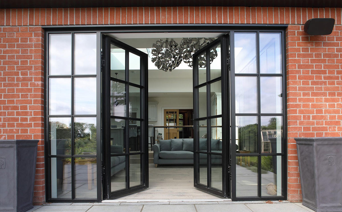 Black Crittall style double French doors with glass sidelites installed on brick exterior wall Black Crittall style double French doors with glass sidelites installed on brick exterior wall