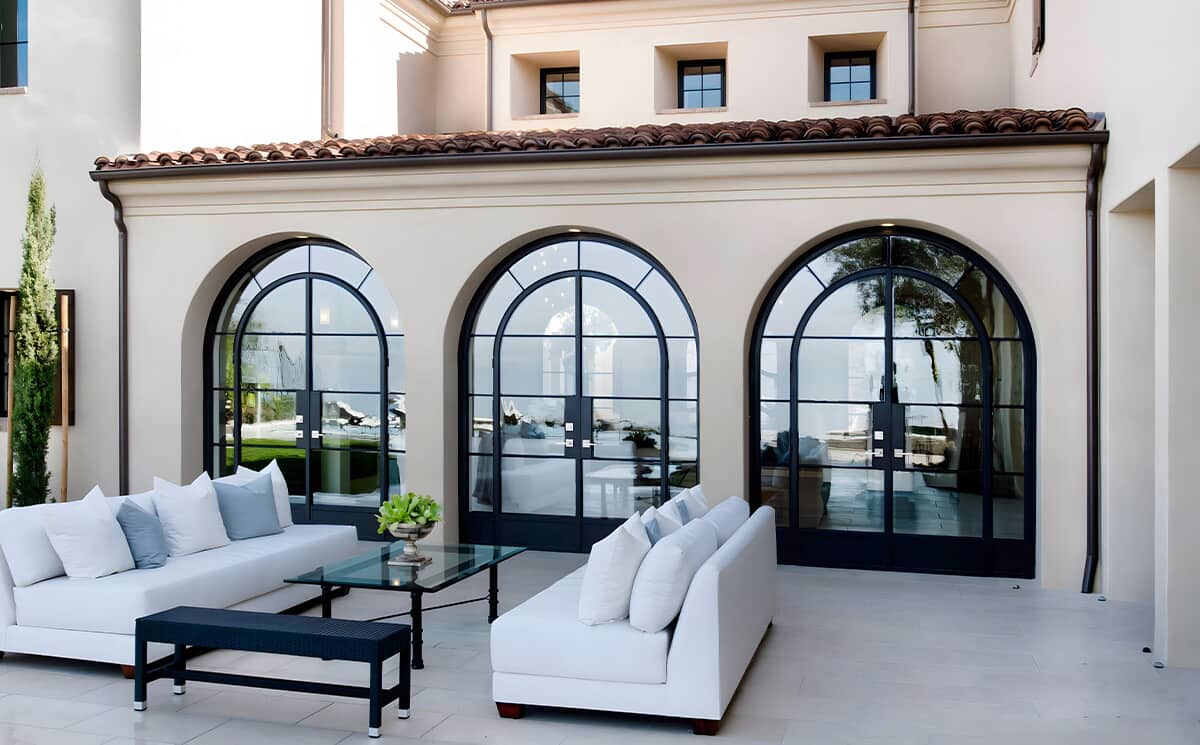 French style arched ultra slim frame black metal glass French swing doors set in a triple arch configuration connecting villa living room to outdoor patio terrace French style arched ultra slim frame black metal glass French swing doors set in a triple arch configuration connecting villa living room to outdoor patio terrace