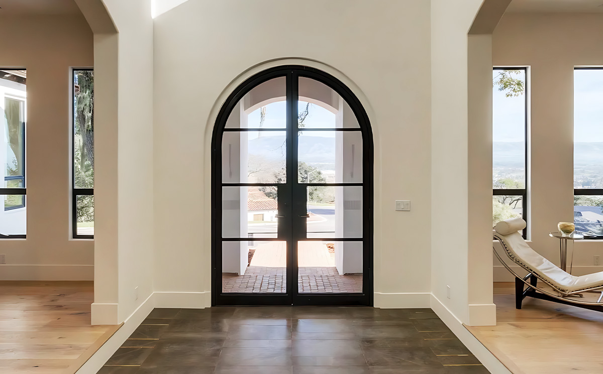 French style arched slim frame black metal double glass swing door installed in an entry foyer hallway transition with oak hardwood flooring French style arched slim frame black metal double glass swing door installed in an entry foyer hallway transition with oak hardwood flooring
